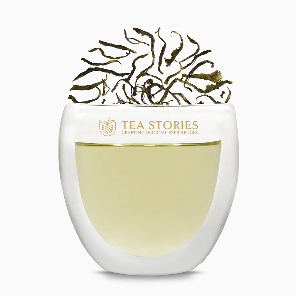 Teastories iconic glass showcasing The Pattumalay Emerald twirl green tea leaves and its light brewed liquor.